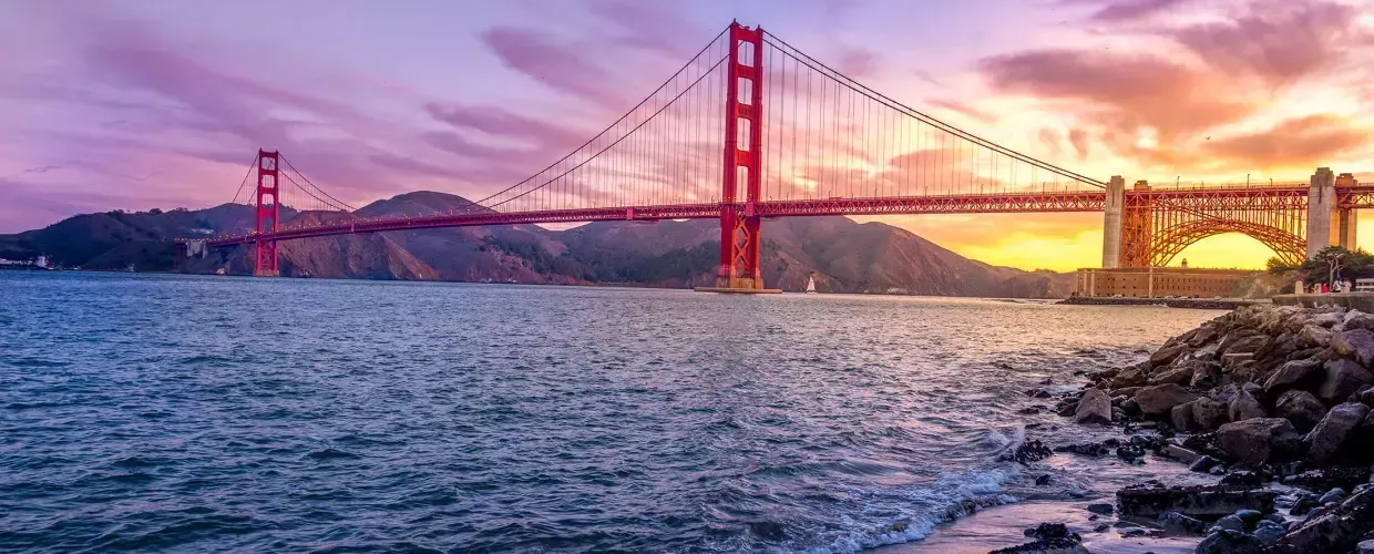 Die 金门大桥 bei Sonnenuntergang mit einem bunten Himmel und der San Francisco Bay im Vordergrund.